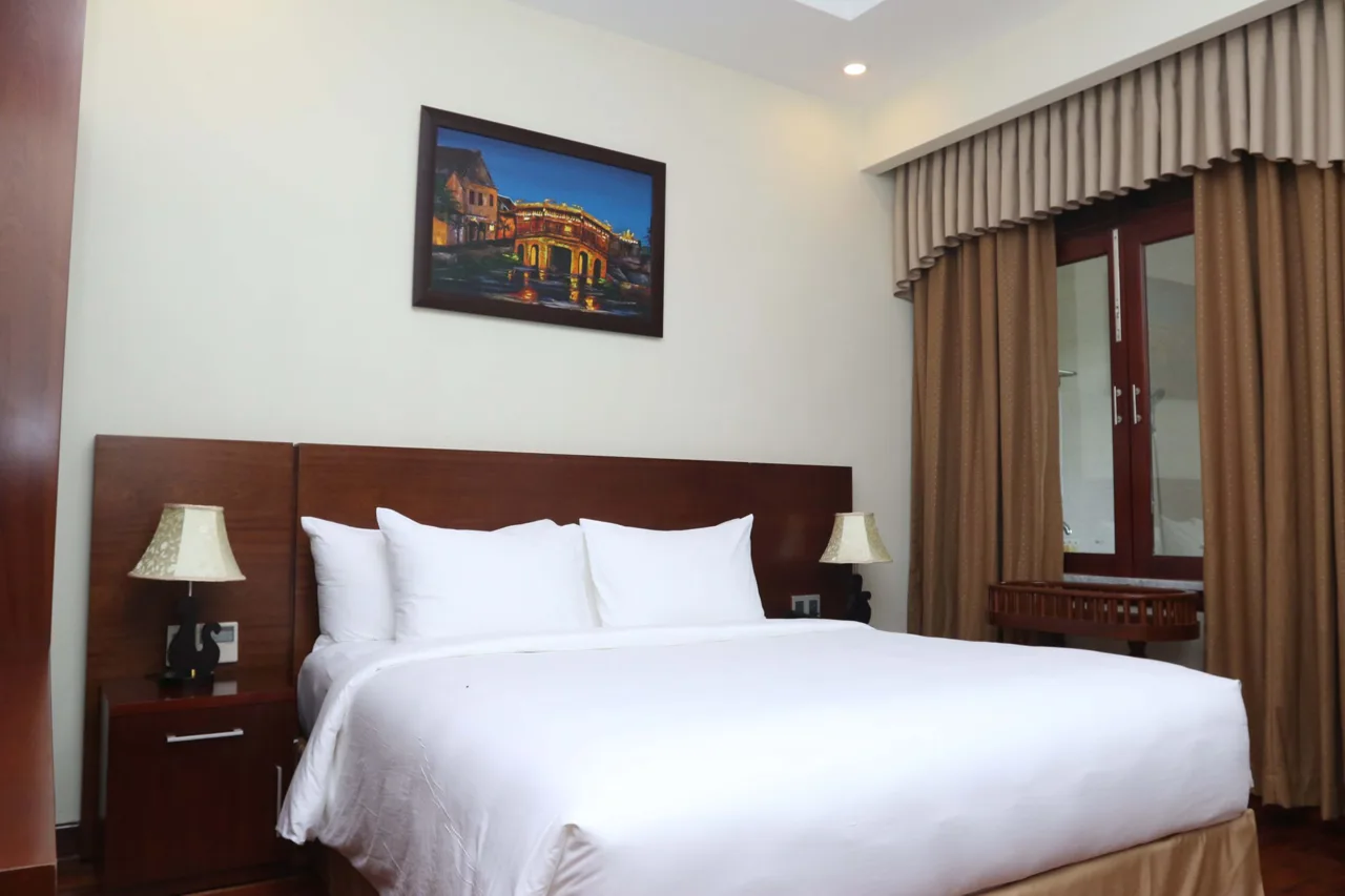 Giường đôi ga trắng, đầu giường gỗ và tranh treo tường